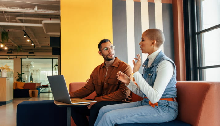 A man and a woman discussing something over a laptop in a bright office