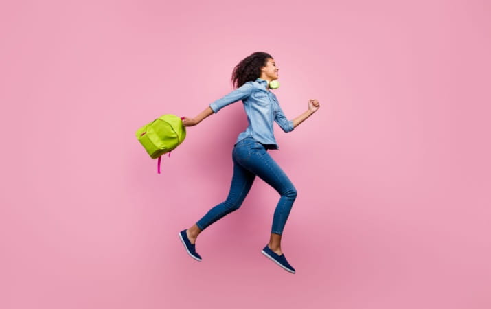 Fastest way to become a teacher Woman in jeans and a shirt running with backpack in hand on pink background