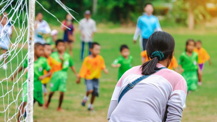 The back of a mum watching and cheering her son playing soccer