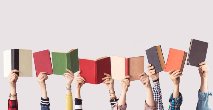 Different peoples' hands playfully holding up a collection of colourful textbooks